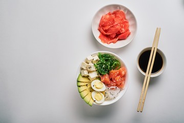 poke bowl with salmon,avocado rice,Chuka Salad,sweet onions,quail eggs sprinkled with white and black sesame with chopsticks,pickled ginger and soy sauce isolated on white background top view flat lay