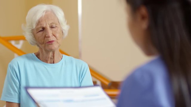 Medium shot of elderly woman having conversation with unrecognizable female physical therapy specialist with clipboard