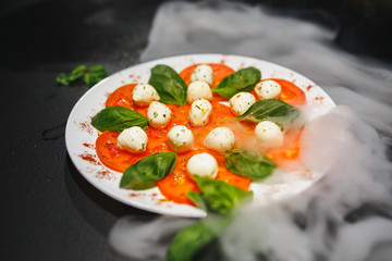 Tomatoes with mozzarella and rosemary on white plate isolated on black background. Close up