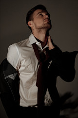 A tired businessman stands in a shirt with taking off jacket and untied his tie.