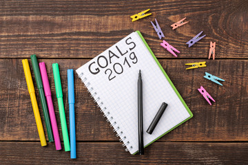 Goals for 2019. Text on notepad with felt-tip pens on a brown wooden background.