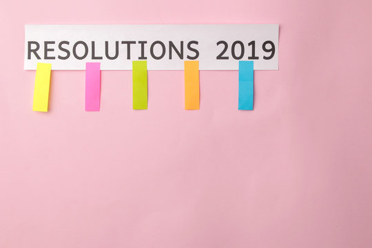 Resolution 2019. Text on a piece of paper with colored stickers on a bright pink background.