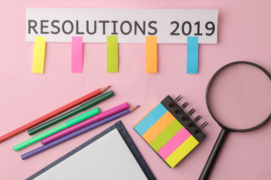 Resolution 2019. Text on a piece of paper with color stickers, pencils and a magnifying glass on a bright pink background.