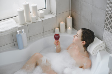 Young woman relaxes in a hot bath full of foam.
