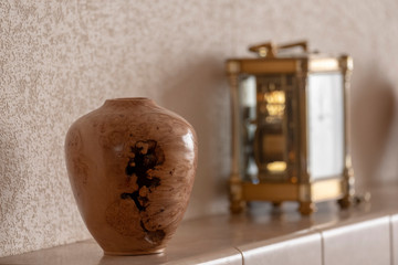 Turned elm burr vase positioned on tiled mantle piece with antique clock in background.