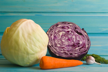 White cabbage, red cabbage, carrots, garlic and dill on blue wooden background.