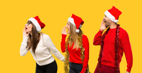 A group of people Blonde woman dressed up for christmas holidays shouting to the lateral and announcing something on yellow background