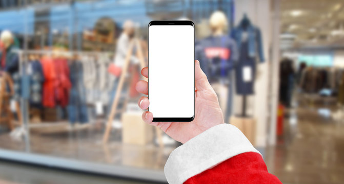 Santa Claus holding smartphone with isolated screen in front of clothing store. Christmas shopping concept