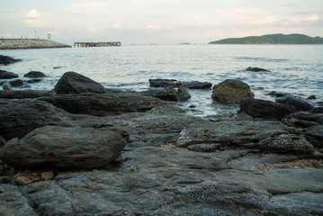 Smoothened stone shores of Khao Laem Ya during a blue sunset, pier in the background. Rayong, Thailand.