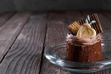  A biscuit cake is sprinkled with cocoa with chocolate cream, a heart of white chocolate, a slice of chocolate tile  and a delicious waffle on wooden background.