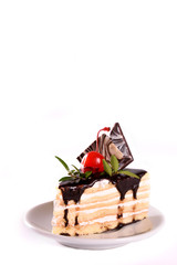 A biscuit cake is filled with chocolate with slices of chocolate tile, cherry and green leaf  isolated