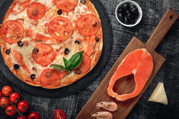 Pizza with cheese, trout, tomatoes, olives and shrimps on chalk board.