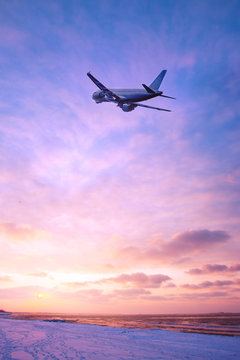 Airplane in the sky over the snowy beach at sunset