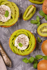 Obraz na płótnie Canvas Delicious healthy tartlets filled with cheese cream and topped with kiwi slices in swirl and chia seeds. Healthy dessert concept.