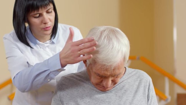 Medium shot of female physiotherapist helping elderly man doing neck exercise to relieve pain