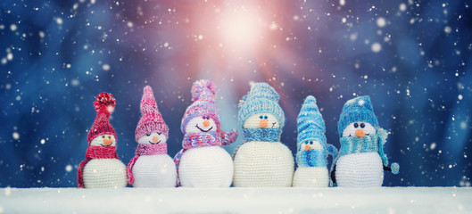 little knitted snowmans on soft snow on blue background