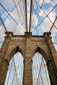 Scenic abstract view of the steel cables and textured bricks of the iconic stone arch tower of the Brooklyn Bridge under soft blue sky with sunset clouds