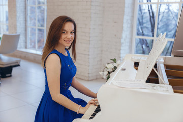 Closeup portrait of a girl in blue dress sitting at the piano and play the piano