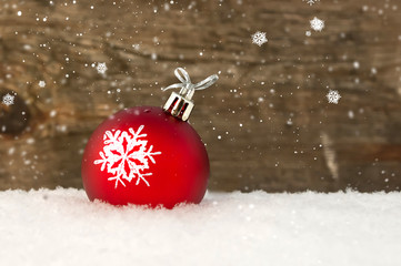 Red Christmas ball in snow on wooden background