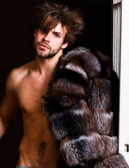 Sexy macho tousled hair coming out bedroom door. Richness and luxury concept. Bachelor rich lover. Guy attractive posing fur coat on naked body. Luxury lifestyle and wellbeing. Luxury status symbol