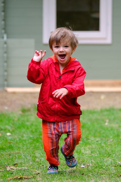 Boy aged two (2) with ecited expression on face as he runs in red coat outside in garden