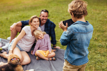 Naklejka na ściany i meble Son photographing family during picnic at park