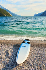 Windsurfing board lying on an empty stony beach by the lake Garda (Lago di Garda), Italy