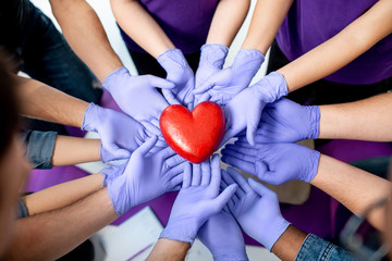 Group of people holding with hands in medical gloves red heart model. Close-up view. Healthy heart...