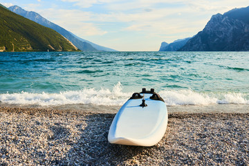 Windsurfing board lying on an empty stony beach by the lake Garda (Lago di Garda), Italy