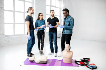 Fototapeta premium Young people standing and talking together during the first aid training with medical stuff and dummies on the floor