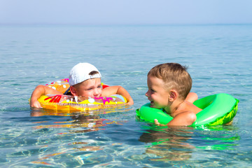 Two happy kids swim on the inflatable circles in the sea in the summer