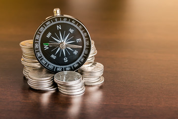Stack of coins with compass on wood table