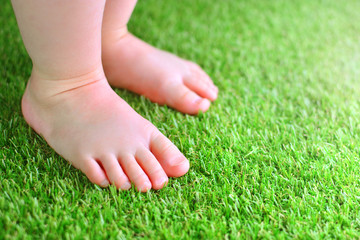 Artificial grass background. Tender foots of a baby on a green artificial turf floor.
