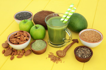 Fresh fruit juice health drink with matcha, flax, chia and hemp seed, nuts and fruits on yellow wood background. High in omega 3, antioxidants, vitamins and dietary fibre.