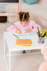 high angle view of cute child writing with pencil while studying at home