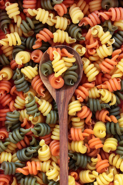 Trotolle tricolour pasta on an olive wood spoon and loose forming an abstract background.