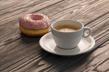 Pink doughnut and a cup of coffee in the morning light.