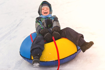 Fototapeta na wymiar Baby boy rolling in the snowy slide on a tubing. Cheerful handsome boy riding a roller coaster.