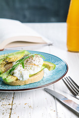 Tost with avocado and poached egg on a blue plate. Fresh and healthy breakfast with avocado toast and orange juice with a book. Healthy food. Morning breakfast. Copy space for text, logo or brand.