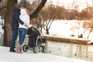 Happy young family walking in a winter park, mom, dad and son in stroller.