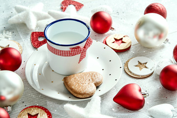 Christmas decoration with a mug of milk plate with gingerbread snowflakes and baubles on a white silvery table.
