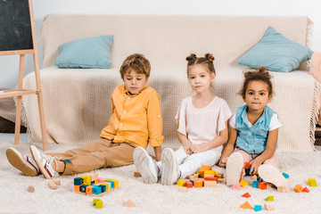 cute multiethnic kids playing with colorful cubes and looking at camera