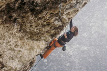 woman climbs grey-color rock in orange pants