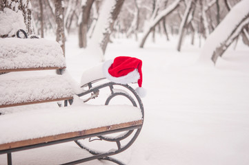 Santa Claus hat, resting on the bench in snow. Christmas celebrate concept