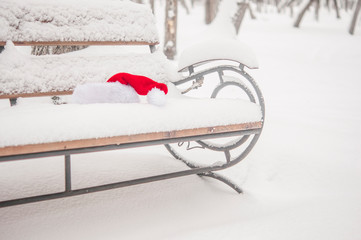 Santa Claus hat, resting on the bench in snow. Christmas celebrate concept