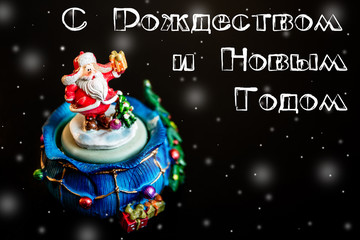 Cute toy Santa Claus isolated on black background with white inscription on Russian language with snowflakes