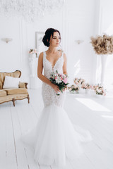 A bride in a white dress is holding a beautiful wedding bouquet. The bride is waiting for the groom in the white room.