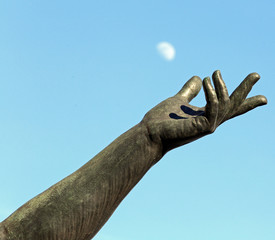hand of statue trying to catch the moon in the sky