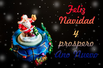 Cute toy Santa Claus isolated on black background with snowflakes and color inscription merry christmas and happy new year in Spanish