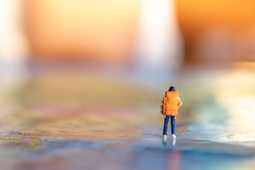 Travel Concept. Woman traveler miniature figures with backpack walking on world map under sunlight.